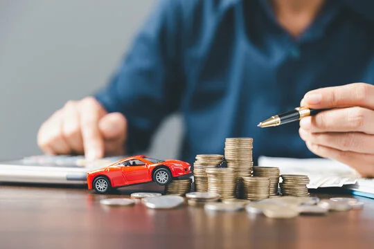 Person calculating car expenses with coins and toy car on desk, concept of auto finance and budgeting.