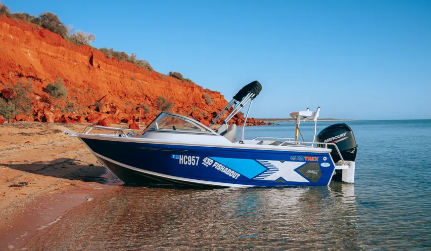 Blue motorboat on a calm beach near red cliffs under clear skies.
